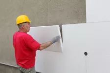 A man wearing a hard hat installs polystyrene insulation