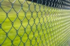A chain link fence in front of a green field, providing a boundary between the field and its surroundings.