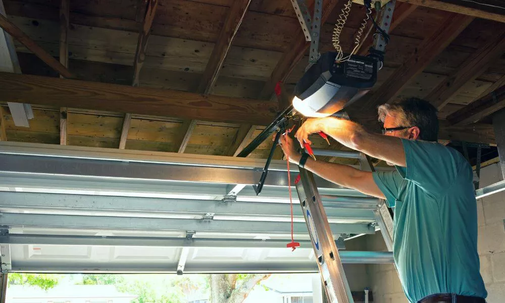 A man using a ladder to fix a garage door opener