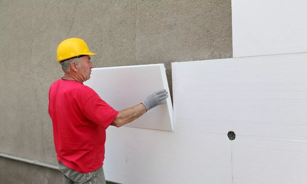 A man wearing a hard hat installs polystyrene insulation