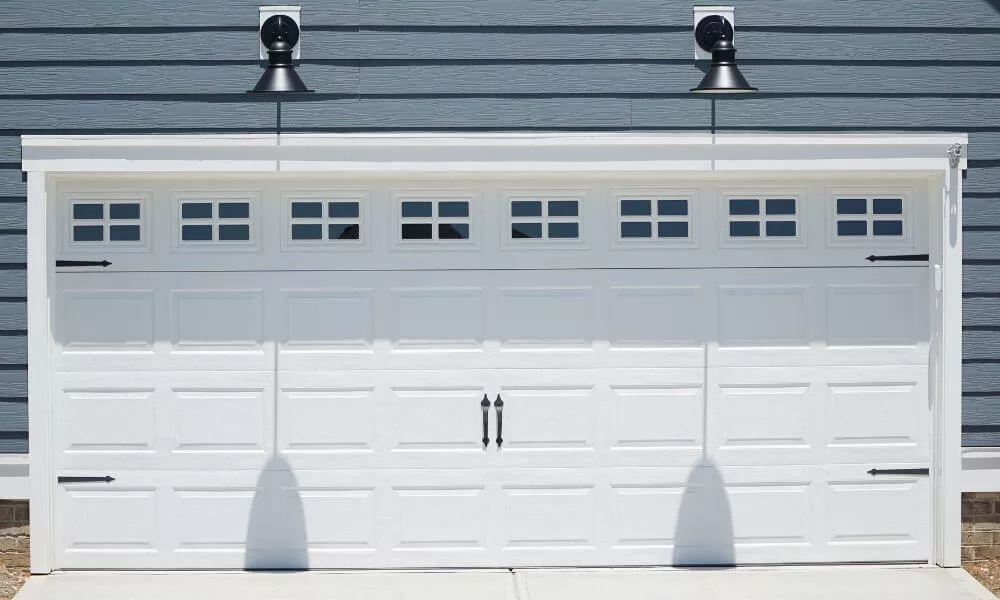 White double garage door with windows and decorative hardwares on a blue house