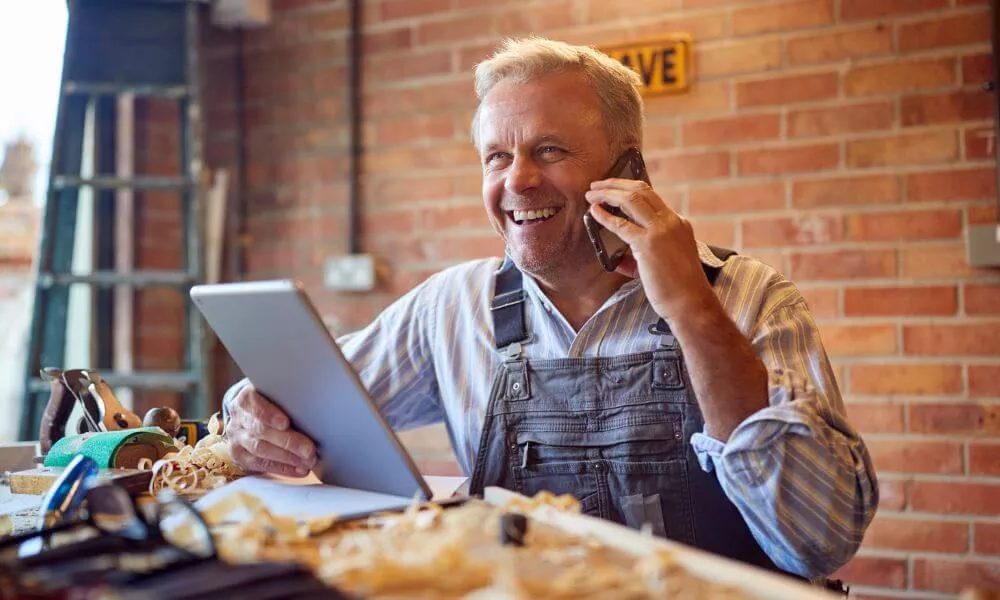 A man sitting at a table, using a laptop and talking on the phone.